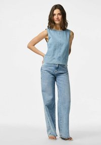 Svijetloplavi traper top bez rukava s uskim strukom, uparen sa širokim svijetloplavim trapericama koje imaju blago izblijedjeli izgled i sirovi rub.