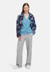 Oversized, fuzzy marineblauwe en grijze jas over een lichtblauwe gestructureerde gebreide cardigan. Grijze sportbroek en witte sneakers maken de outfit compleet.