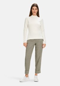 Weißes Langarmoberteil mit Stehkragen, kombiniert mit grauen gemusterten tapered Hosen und weißen Slippern. Einfaches, elegantes Design.