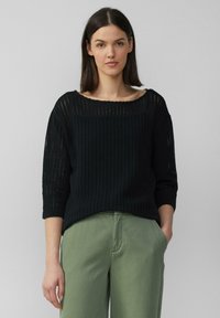 Zwarte, opengehaakte trui met driekwartmouwen en een ruime halslijn, gecombineerd met lichtgroene broek. Heeft een relaxte fit en een gestructureerd design.