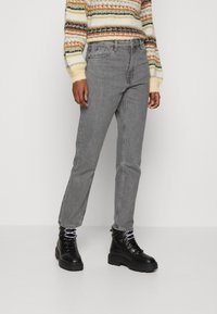 Jeans rectos grises de denim, con una cintura de altura media. Combinados con botas negras gruesas de cordones y un suéter de rayas multicolores.
