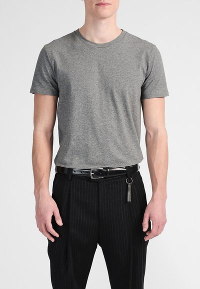 T-shirt en coton gris à manches courtes, col rond, associé à un pantalon noir à rayures et une ceinture noire avec un grelot décoratif.
