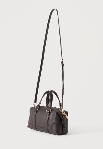 Sac à main en cuir marron foncé avec des poignées courtes, une longue bandoulière réglable et une quincaillerie dorée.