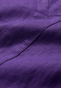 Violetti pellava-kangas pehmeällä, tekstuurillisella pinnalla ja hienovaraisella kiillolla, jossa näkyy ompelujälkiä ja taitteita syvyyden lisäämiseksi.