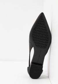 Schwarzer High Heel mit spitz zulaufender Zehenpartie und Ausschnittdesign. Verfügt über eine strukturierte Gummisohle und ein glattes Obermaterial.
