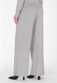 Šedé široké kalhoty vyrobené z měkké tkaniny, s žebrovanými manžetami a klasickým zakončením. Spárovány s černými lodičkami se špičatou špičkou.