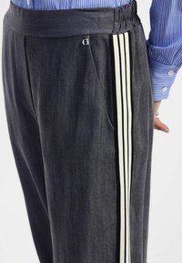 Pantaloni grigi scuri con vestibilità comoda, vita elasticizzata e dettagli laterali a righe bianche con un piccolo logo.