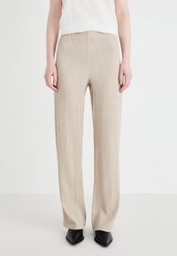 Beige plisserte vide bukser med elastisk midje, myk tekstur og flytende design, kombinert med svarte spisse sko.