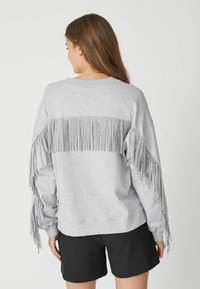 Grauer Sweatshirt mit Fransendetails an den Ärmeln und am Rücken, mit einem lässigen Schnitt und rundem Ausschnitt, kombiniert mit schwarzen Shorts.