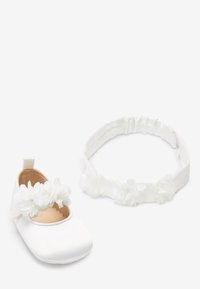 Zapato de bebé blanco con correa de flor de tela y diadema floral blanca a juego con respaldo elástico, ambos suaves y decorativos.