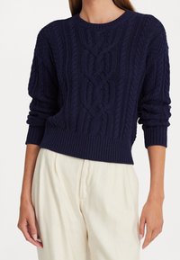 Pull en maille torsadée bleu marine avec un col rond et des poignets et ourlet côtelés. Caractérisé par un motif texturé et une coupe légèrement ample.