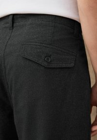Close-up of dark pinstriped trousers with a buttoned back pocket flap, worn with a white shirt.