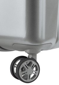 Valigia rigida argentata con finitura testurizzata, dotata di ruote nere resistenti e un design moderno delle ruote per una mobilità fluida.