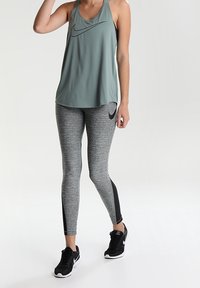 Lichtgroen sportief tanktop met zwart Nike-logo, gecombineerd met grijze melange legging met zwarte zijpanelen, aangevuld met zwarte sneakers.