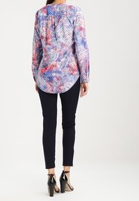 Long-sleeve blouse with a multicolored paisley pattern in pink, blue, and white; rounded hem; paired with dark slim-fit pants and black heels.