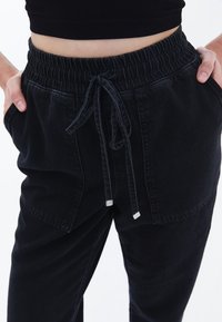 Pantalones jogger de mezclilla negra con cintura elástica, cierre de cordón, dos bolsillos laterales y un corte relajado. Textura suave con un diseño minimalista.