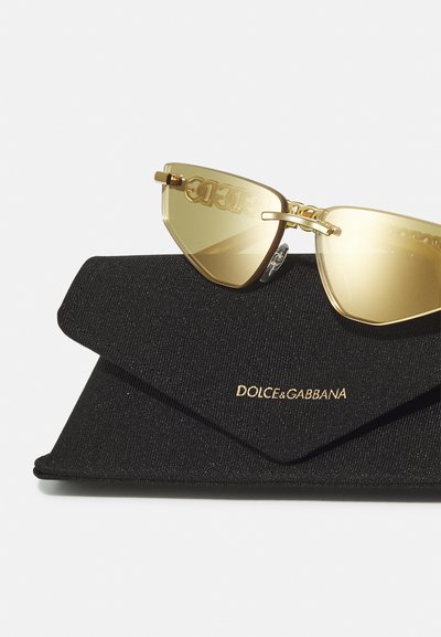 Gafas de sol estilo gato en tono dorado con lentes amarillos, con detalles del logo en las lentes, reposando sobre un estuche de tela negra grabado con "DOLCE&GABBANA."