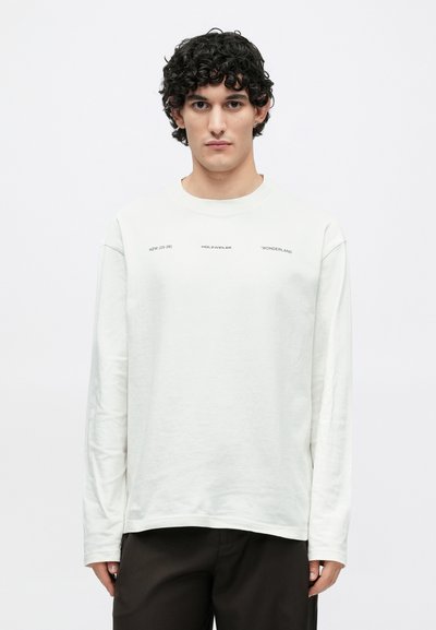 T-shirt branca de manga comprida feita de algodão macio com gola redonda, apresentando texto impresso no peito em letras maiúsculas pretas.