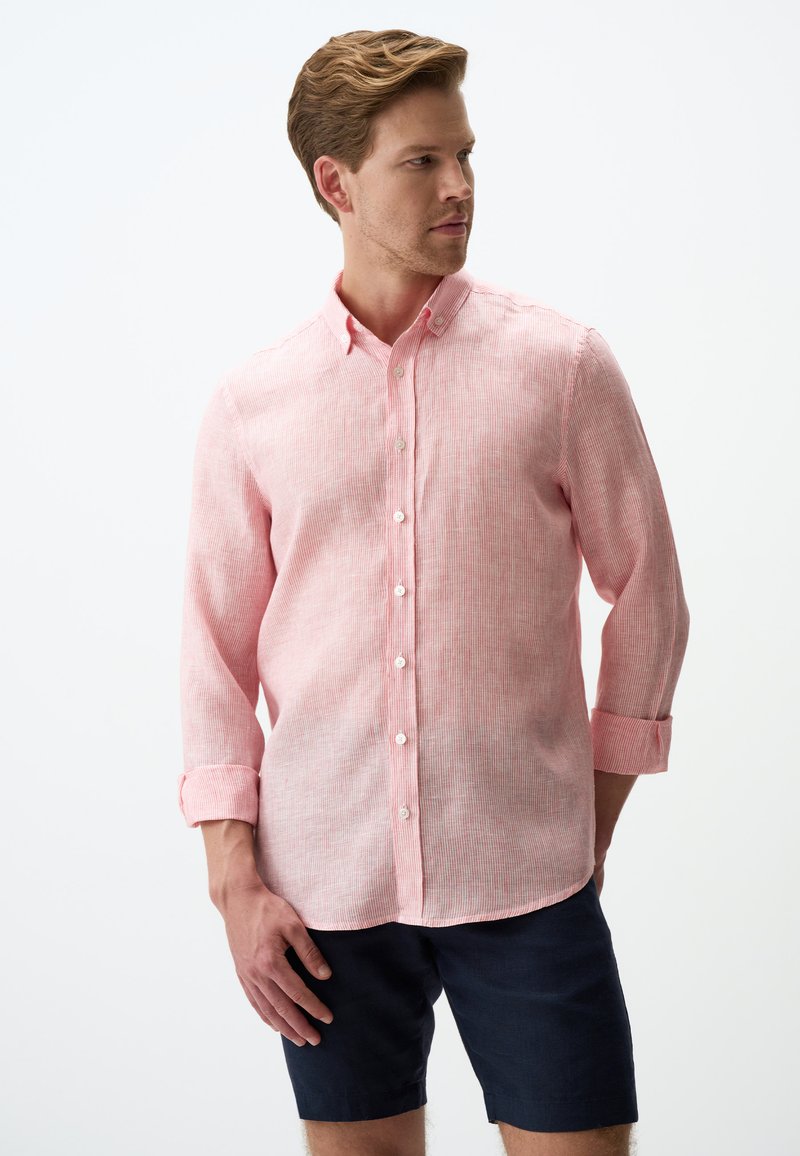 Helles rosa Hemd mit subtiler Textur, langärmlig und hochgekrempelt, kombiniert mit dunklen Shorts.