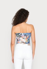 Top cropped sem alças com um design impresso colorido apresentando elementos abstratos. Feito de um tecido elástico, combinado com calças brancas de cintura alta.