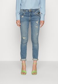 Ljust blå denimjeans med slim fit, slitna detaljer och uppvikta fållar. Matchas med gröna sandaletter med hög klack och remmar.