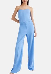 Jumpsuit senza spalline di color azzurro chiaro con un corpetto aderente e pantaloni ampi e fluidi. Il tessuto appare liscio con un dettaglio di cintura strutturata in vita.