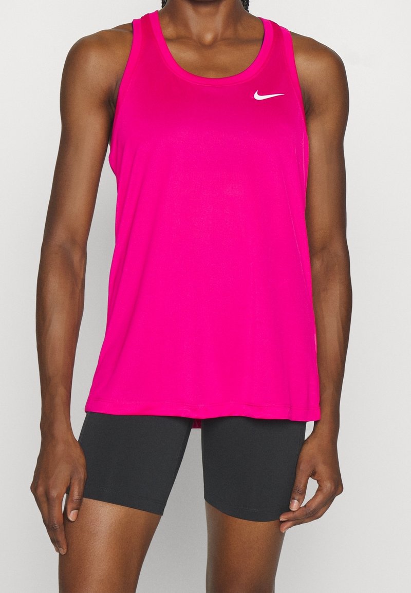 Vaaleanpunainen Nike ilmanhiha tankkitoppi, jossa on pyöreä pääntie, ja vasemmassa yläkulmassa pieni valkoinen logo. Yhdistetty mustiin shortseihin.