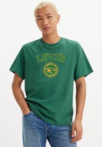 Grønn bomull t-skjorte med en stor gul "LEVI'S"-logo og sirkulært grafisk design foran, rund hals, korte ermer.