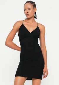 Rochie neagră cu un design ajustat, decolteu în V și bretele subțiri. Fabricată dintr-un material moale și elastic, cu un luciu subtil. Fald scurt.