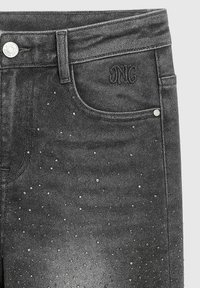 Jeans en denim noir avec un design clouté et des accents argentés. Le tissu a une texture légèrement décolorée, avec un logo brodé visible.