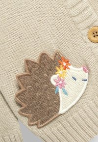 Beige kofta med en applikation av en brun och vit igelkott. Igelkotten har blommig broderi i orange, rosa och blått. Detalj med träknapp.