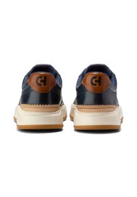 Marinblå läderskor med bruna accenter, vit mellansula och texturerad gummisula. Har en logotyp på hälen och stickade detaljer.