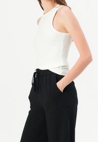 Tank top in ribbed white fabric with a high neckline, paired with black drawstring pants featuring side pockets. Smooth texture, lightweight design.