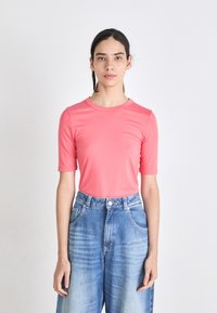 Camisola rosa de manga curta em tecido liso, combinada com jeans de denim azul de cintura alta, com pernas largas e bolsos frontais.
