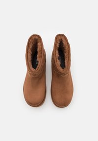 Botas de tobillo de ante marrón con un suave forro de pelo sintético, puntera redondeada y acentos texturizados en el cuello. Suela plana, adecuadas para el uso en invierno.