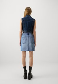 Chaleco de denim con un lavado oscuro, combinado con una falda de denim azul claro. La falda presenta un dobladillo desgatado y dos bolsillos traseros. Botines negros completan el look.