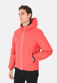 Giacca leggera rossa con cappuccio, zip frontale, due tasche laterali, polsini elasticizzati e una texture morbida. Abbinata a uno strato interno blu.
