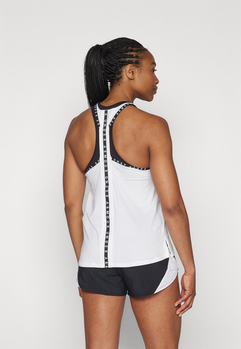 Canotta atletica bianca con accenti neri e logo, design a schiena scoperta, abbinata a pantaloni corti neri con dettagli in rete bianca.
