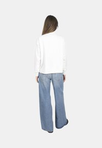 Felpa bianca a maniche lunghe abbinata a jeans blu a vita alta e gamba larga. Texture liscia e design semplice. Vista posteriore.