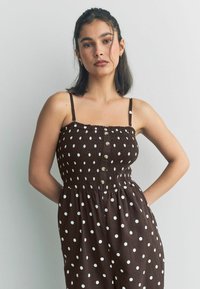 Rochie cafenie cu buline, cu bretele subțiri, având un bust elastic și nasturi pe față. Material moale, cu un design de fustă fluidă.