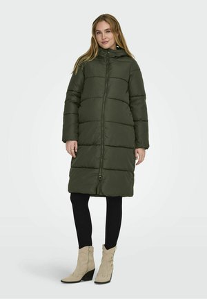 Manteau matelassé vert olive avec fermeture éclair à l'avant, col montant et manches longues. Présente un motif piqué et tombe à mi-mollet. Leggings noirs et bottes à talons beiges.