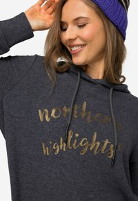 Mørkegrå h�ættetrøje med guldtekst, der læser "northern highlights." Har snøre i hætten og et blødt, struktureret stof.