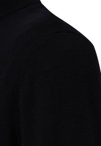 Close-up van zwart gebreide stof met details van de schouder- en mouwnaad op een kledingstuk.