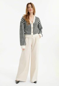 Černobílé houndstooth zkrácené kardigán s krémovými akcenty a knoflíky, kombinovaný s béžovými širokými kalhotami a černými botami.