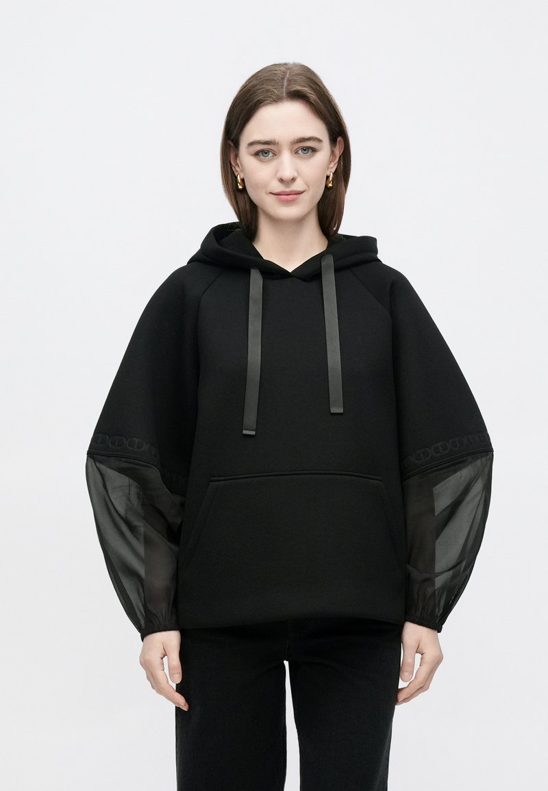 Črna kapucna majica s satenskimi trakovi za nastavitev, z žepom spredaj in prozornimi črnimi rokavi s potiskanim robom.