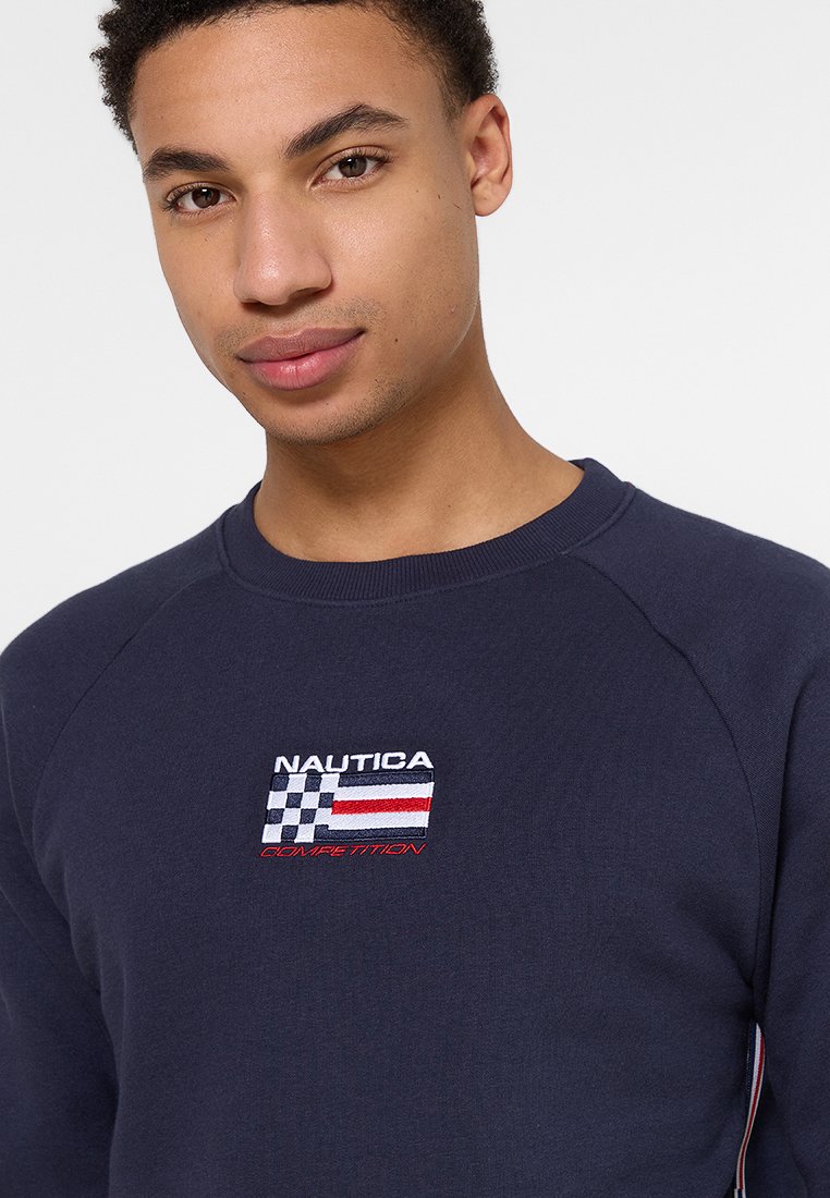 Nautica Sweatshirt in Marineblau mit gesticktem kariertem Flaggen-Design, roten und weißen Akzenten sowie Raglanärmeln; weicher Stoff.