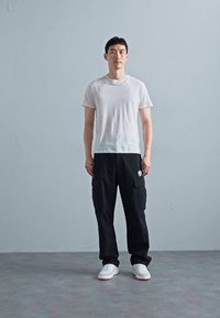 Biała koszulka z okrągłym dekoltem, czarne spodnie cargo z bocznymi kieszeniami i białe sneakersy. Prosty design, luźny krój i neutralna kolorystyka.