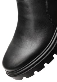 Stivale in pelle nera con punta arrotondata e suola spessa a trazione, mostrando una texture liscia e cuciture dettagliate.