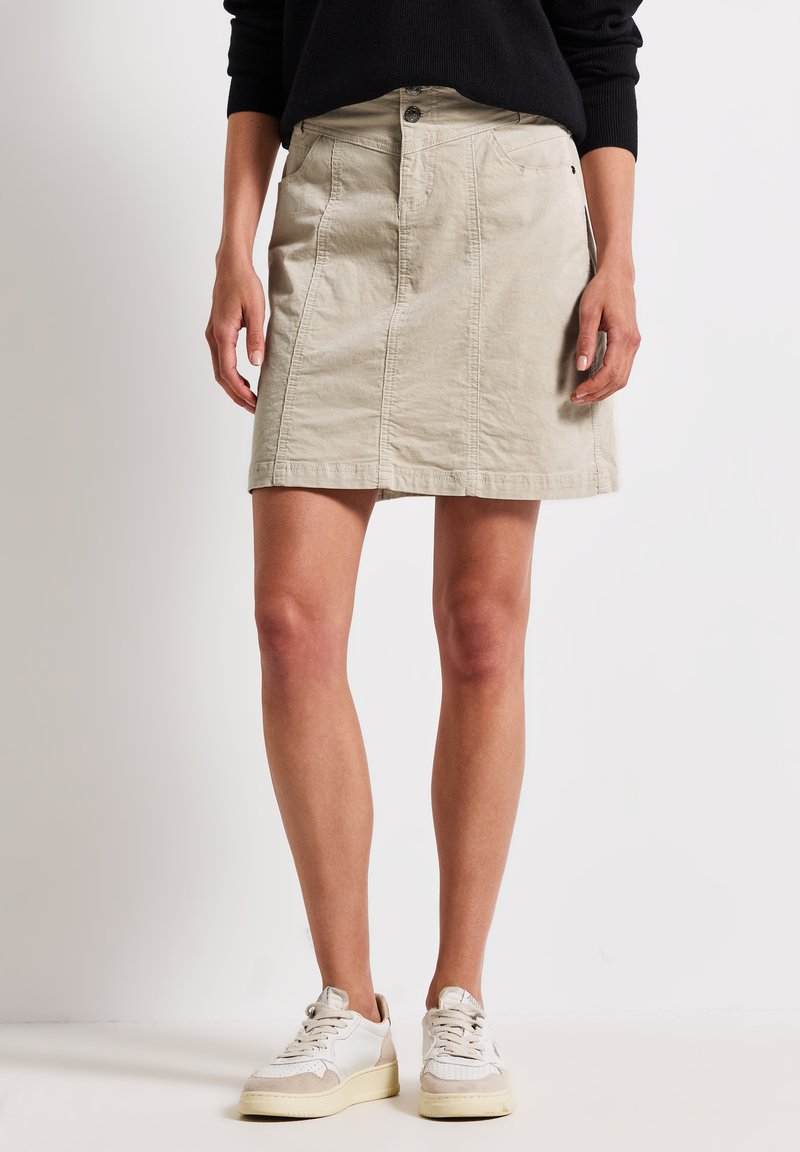 Lichtbeige denimrok met een rechte snit, sluiting met knopen aan de voorkant en zijzakken. Gemaakt in combinatie met witte sneakers. Soepele textuur.