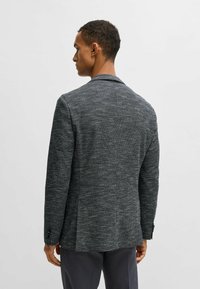 Blazer grigio texturizzato con uno spacco singolo e rever a punta. Caratterizzato da polsini con bottoni e una silhouette sagomata, adatto per abbigliamento formale.